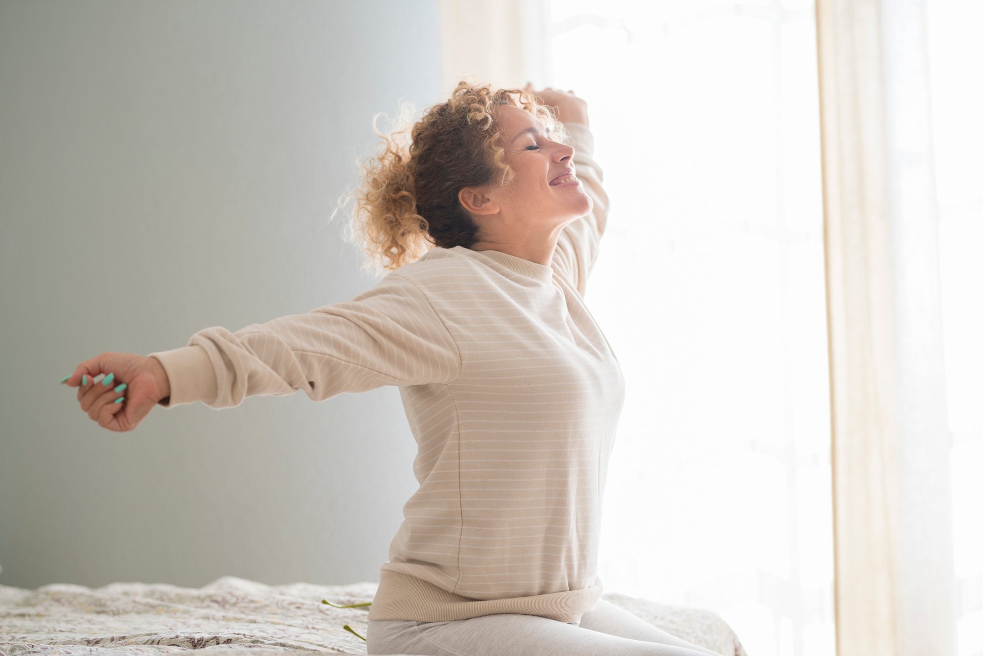 A woman with blonde hair and a white shirt stretches out first thing in the morning.
