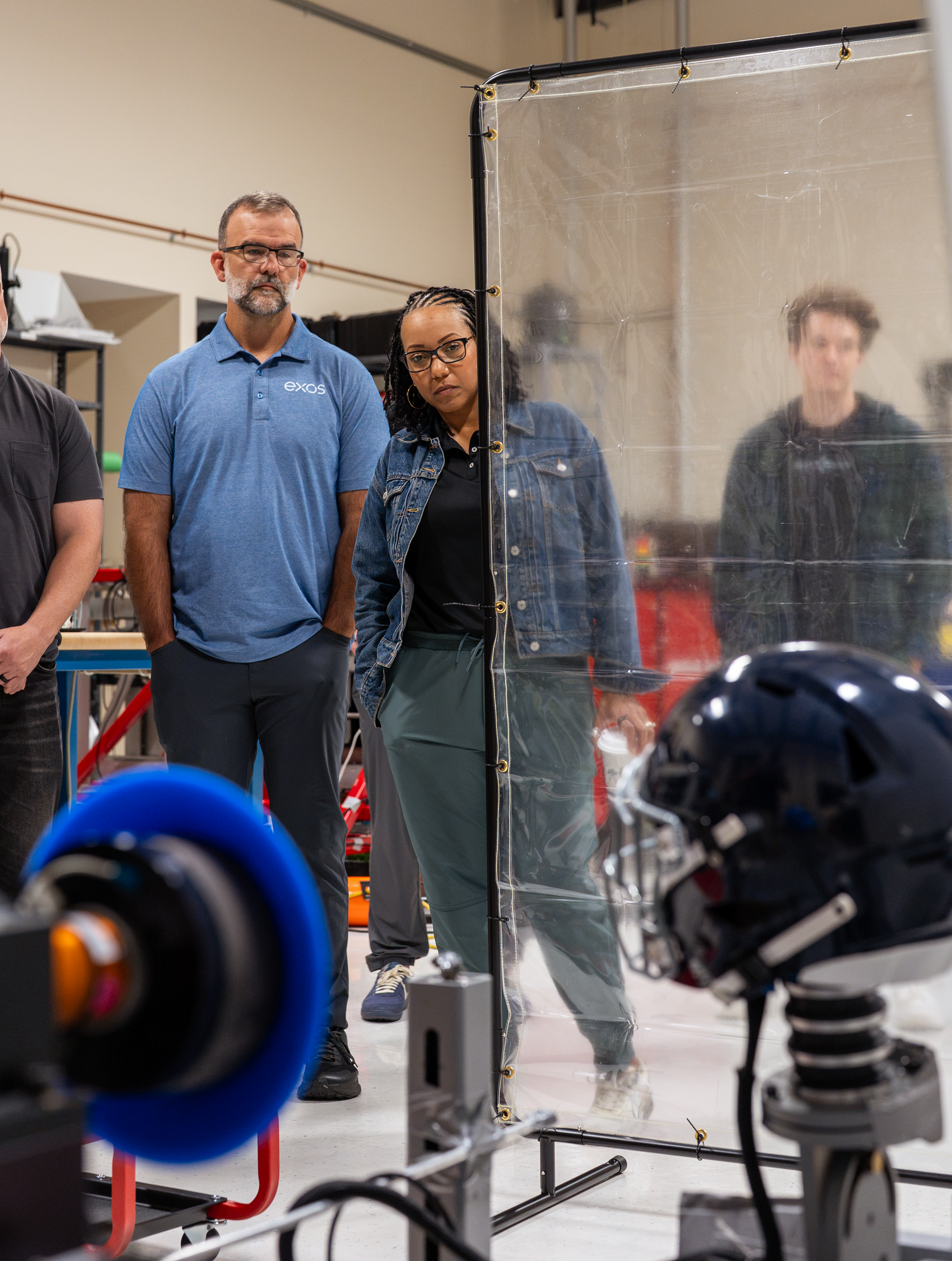 Exos & Biocore teammates stand in front of a helmet safety testing machine.