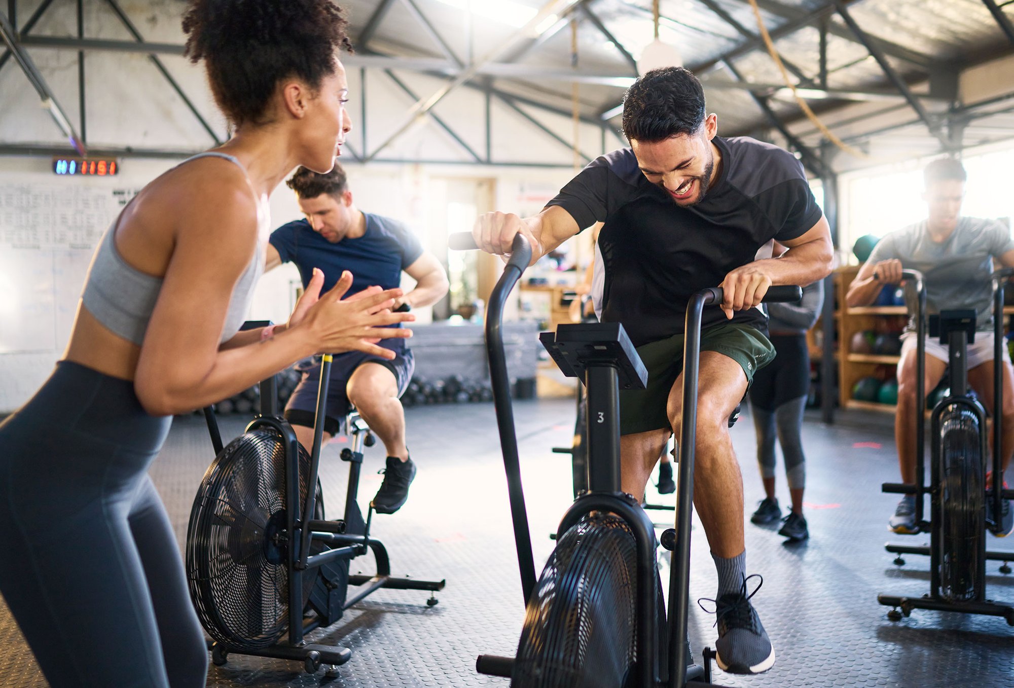 People working out on air bikes in a gym while a coach encourages them.
