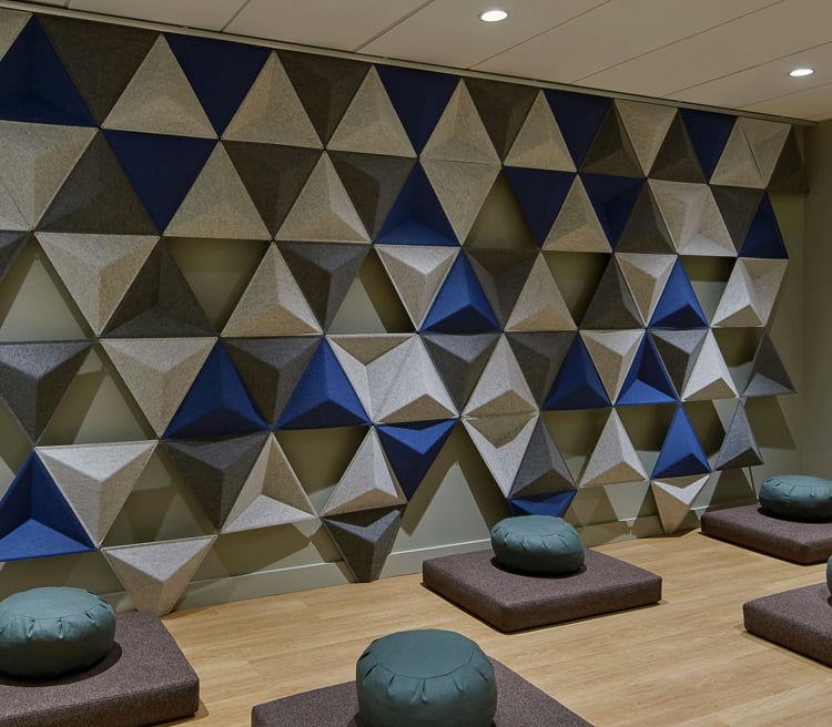 Meditation room with floor cushions and a geometric, sound-absorbing wall design.