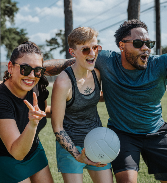 Employees smiling and playing volleyball outdoors, fostering workplace connection, joy, and well-being.