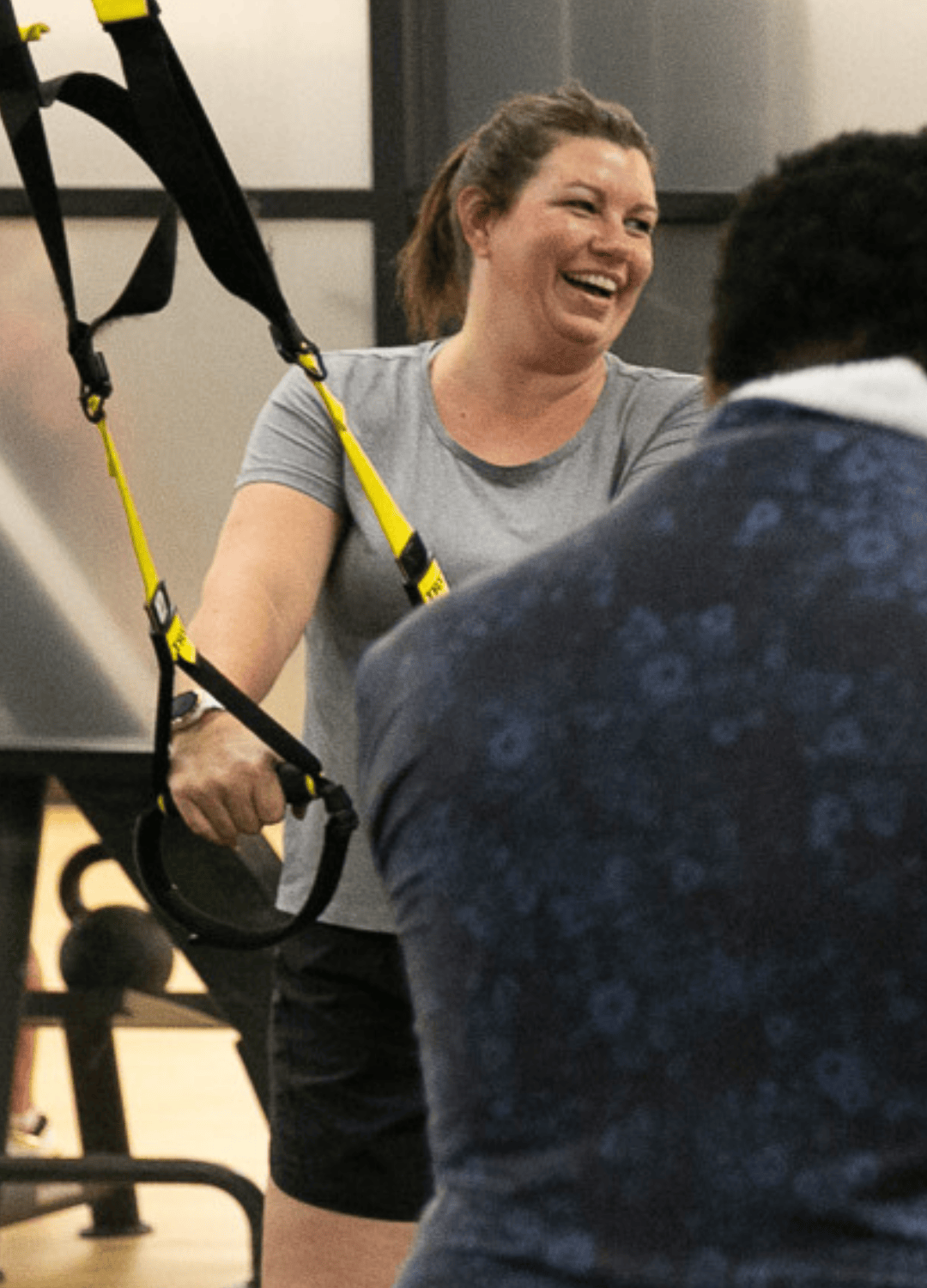 Woman laughs while using suspension straps during a workout session, engaged and energized.