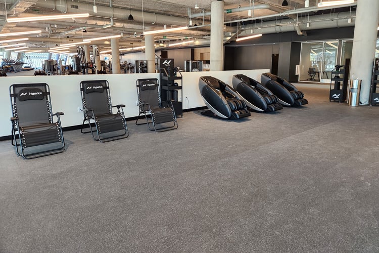 Recovery area in a gym with Hyperice lounge chairs and massage chairs next to open workout space.
