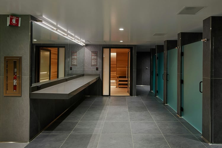 Modern locker room with private showers, sauna entrance, and dark tile finishes.