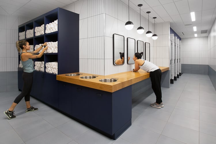 Locker room with modern finishes, showing towel service and vanity area designed for post-workout recovery and care.