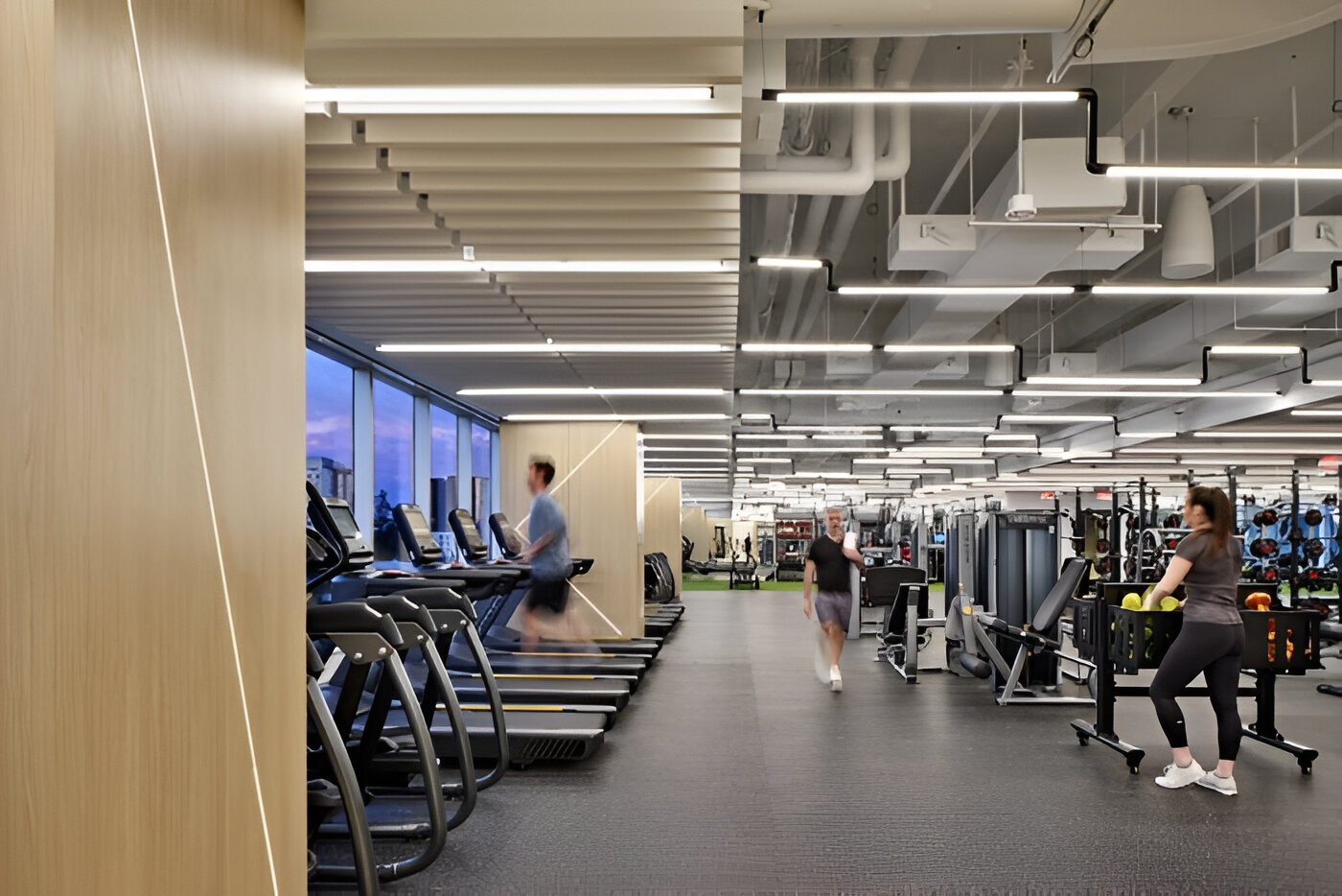 People using treadmills and strength equipment in a spacious, well-lit corporate fitness center.
