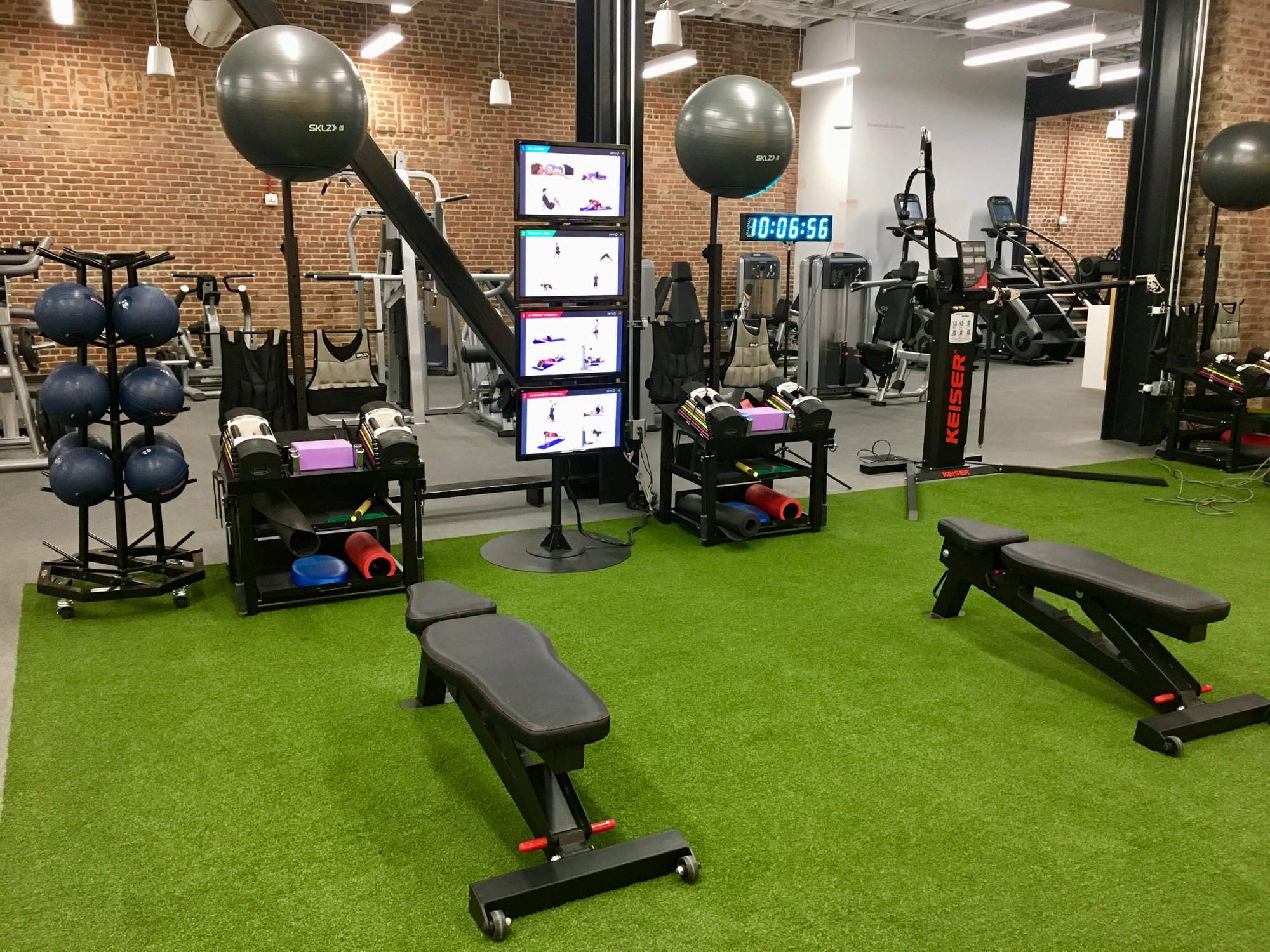Indoor turf training zone with benches, weights, stability balls, and digital workout displays.