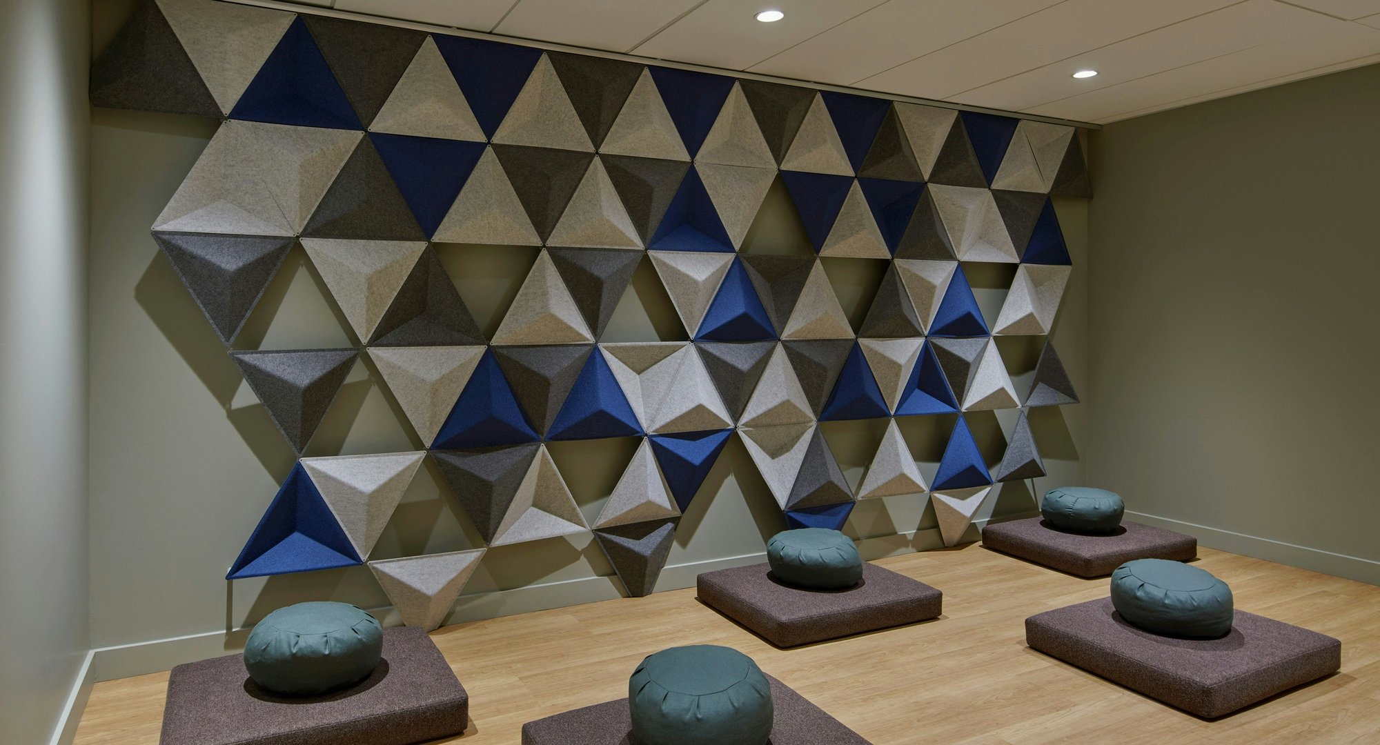 Meditation room with floor cushions and a geometric, sound-absorbing wall design.