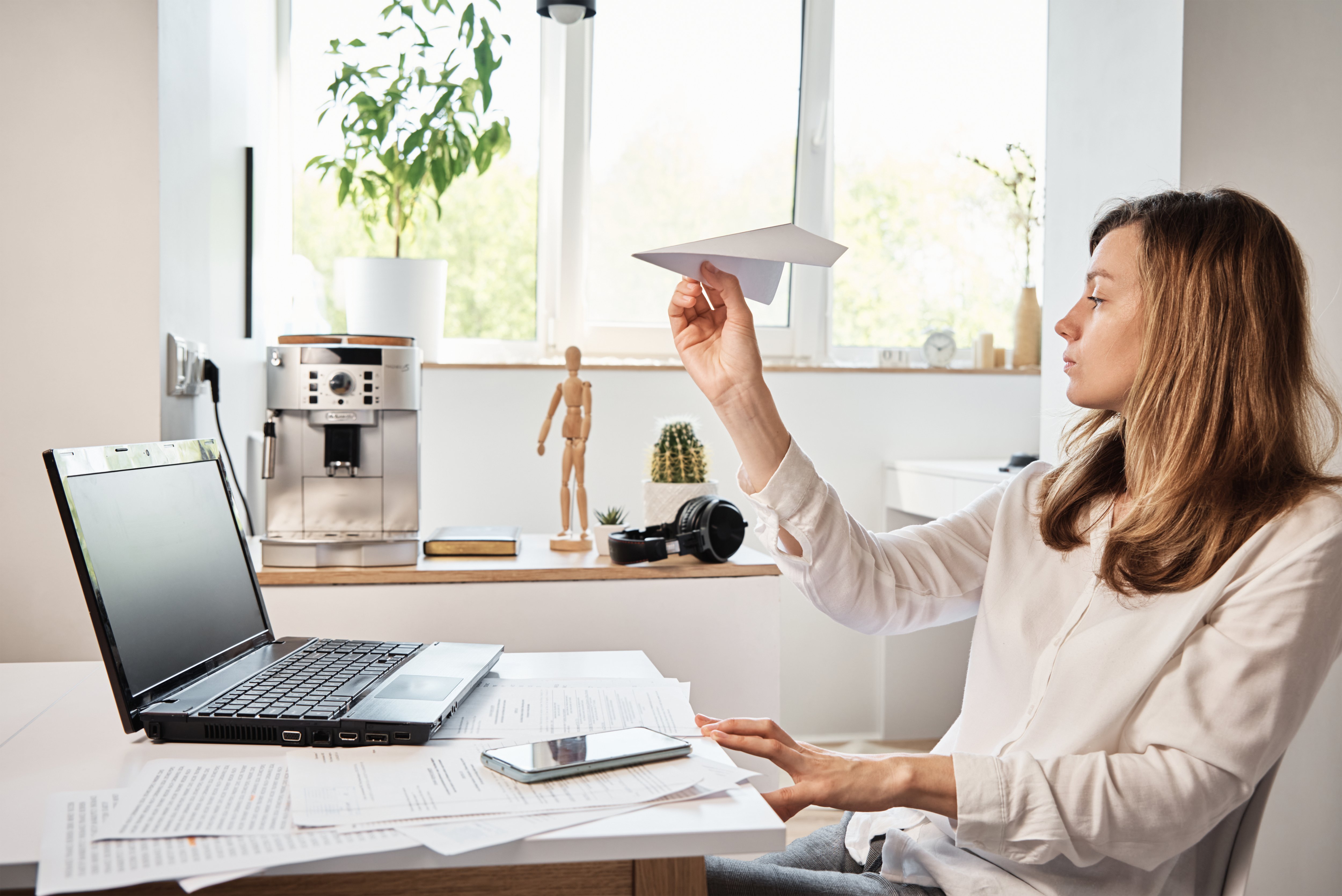 Woman launching a paper airplane at her desk, symbolizing an underperforming employee distracted at work.