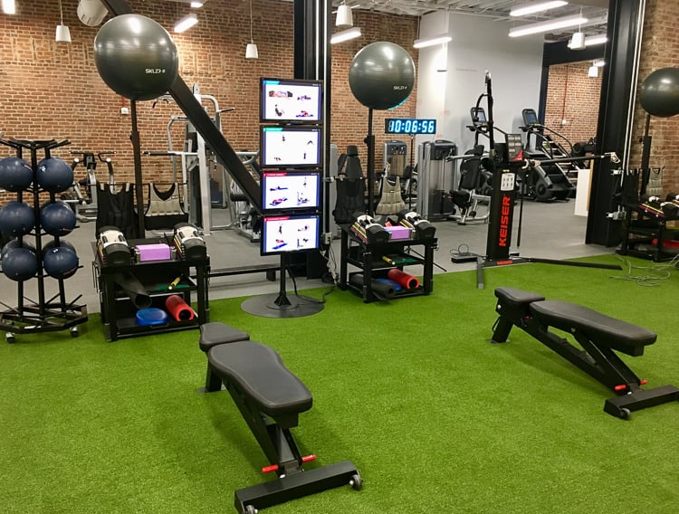 Indoor turf training zone with benches, weights, stability balls, and digital workout displays.-3