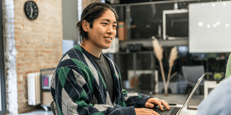 Focused man smiling while typing on laptop, fully engaged in his work.