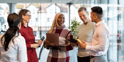 Diverse group of colleagues smiling and talking together in a bright, modern office setting.