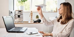 Woman launching a paper airplane at her desk, symbolizing an underperforming employee distracted at work.