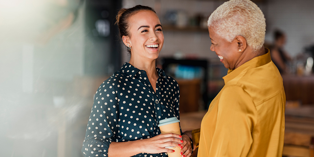 Two women engaged in a chat over coffee in an office.