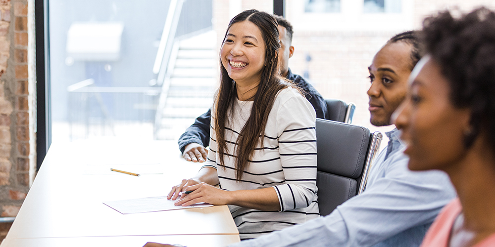 Young professionals seated at a conference table smile and engage during a collaborative workplace session.