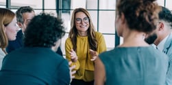 Leader facilitating an engaged team discussion in a modern office, with colleagues listening and contributing in a collaborative setting.