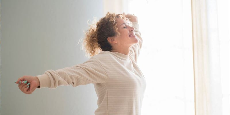 A woman with blonde hair and a white shirt stretches out first thing in the morning.