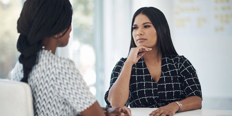 Two women having a focused conversation in a bright office setting, with one actively listening and thoughtfully engaging.