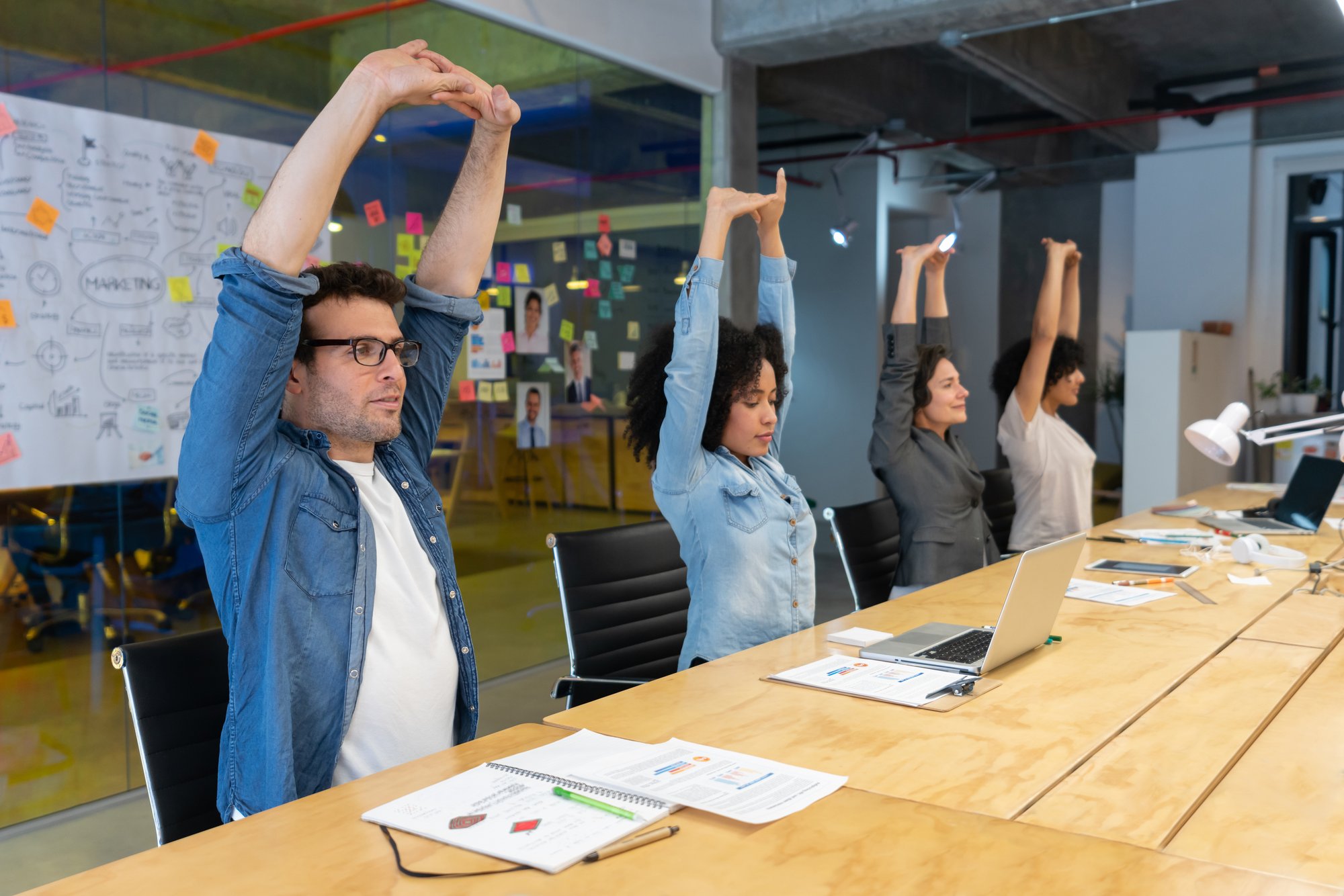 A room of employees stretching at a meeting desk