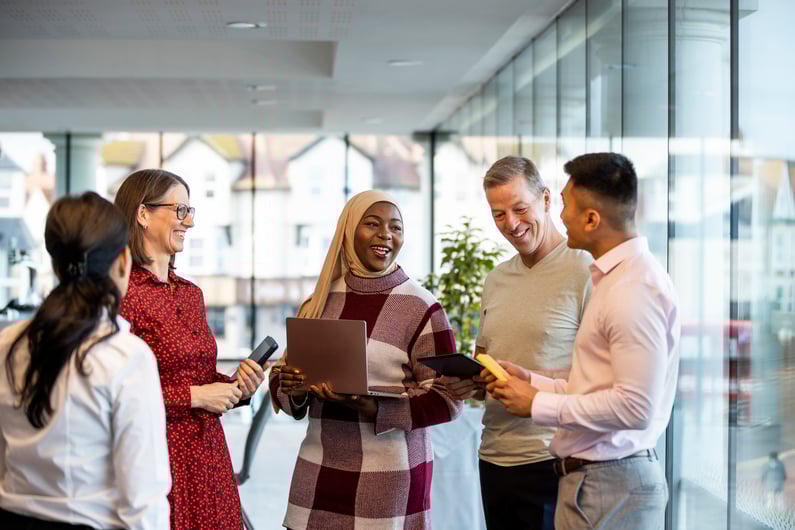 Diverse group of colleagues smiling and talking together in a bright, modern office setting.