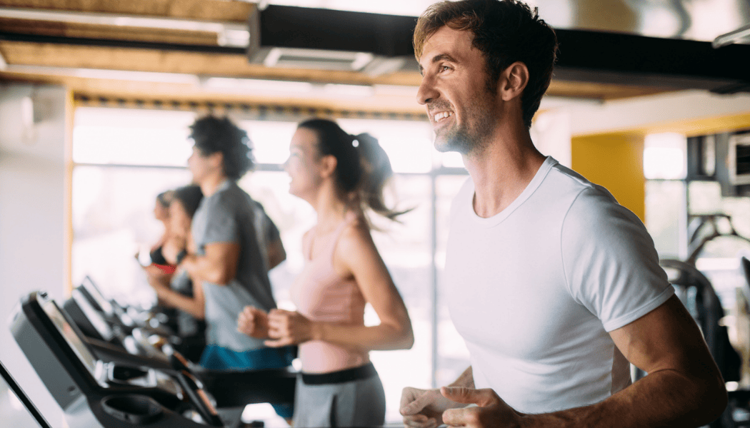 Group of employees running on treadmills in a bright corporate fitness center, smiling and focused during a workout.