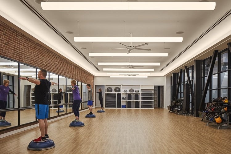 Group fitness class using balance trainers in a mirrored studio with wood floors and natural light.