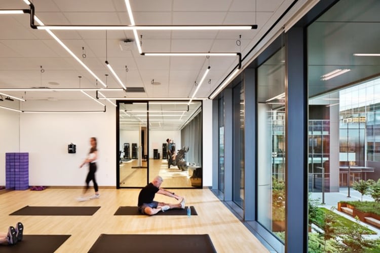 Man stretches on a mat in a modern fitness studio with large windows and natural light