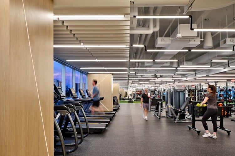 People using treadmills and strength equipment in a spacious, well-lit corporate fitness center.