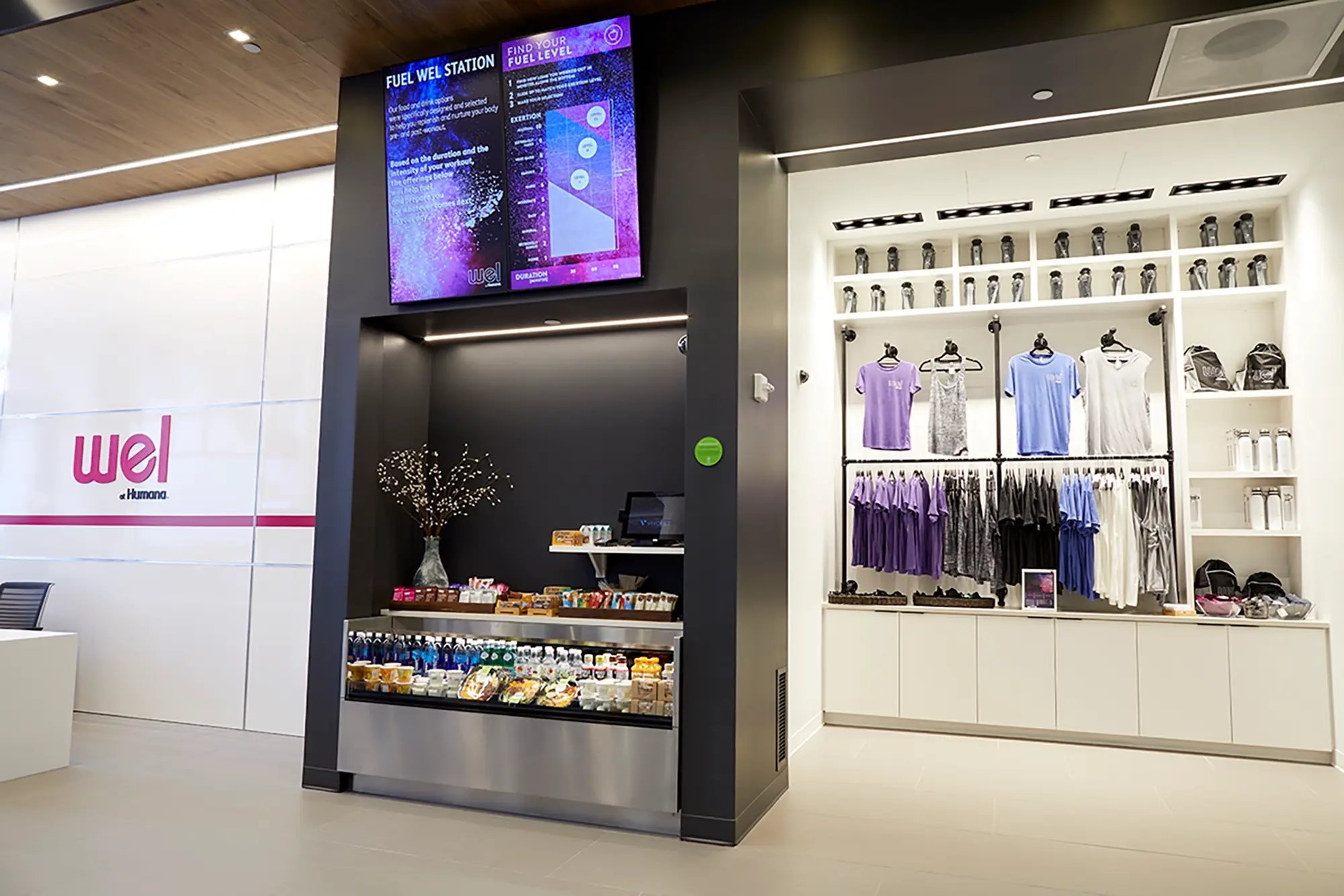 Retail-style wellness station with snacks, supplements, and branded apparel at WEL by Humana