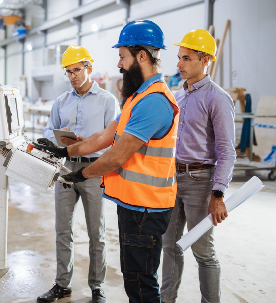 Team of engineers in safety gear reviewing plans on manufacturing floor, highlighting workplace efficiency and collaboration.