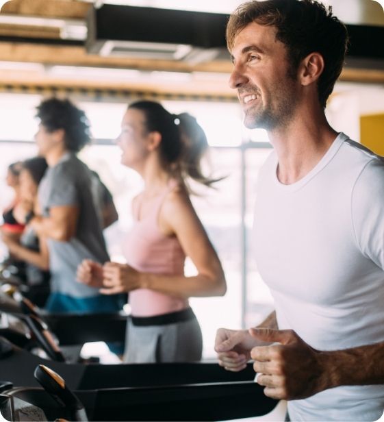 Group of employees running on treadmills in a bright corporate fitness center, smiling and focused during a workout.