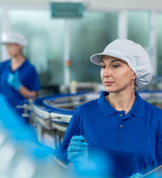Woman in blue uniform and hairnet inspects bottled water on a production line in a factory.