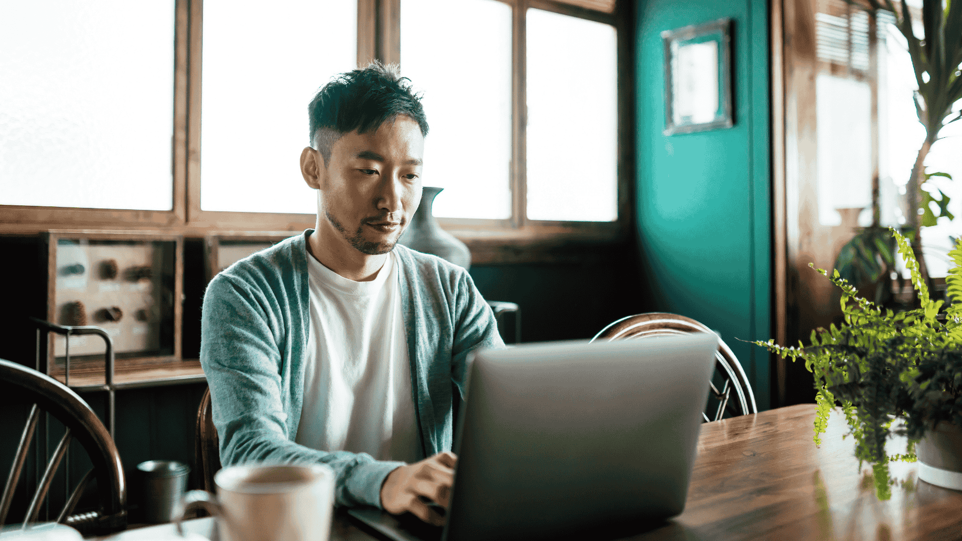 Young man sits at a kitchen table working intently on a laptop.
