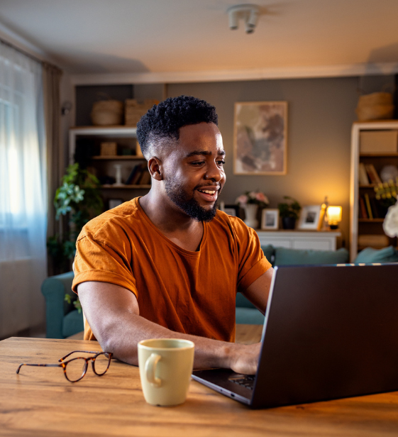 Smiling remote employee in casual clothes works on a laptop at home, representing Exos’s approach to sustaining culture and capacity in distributed teams.